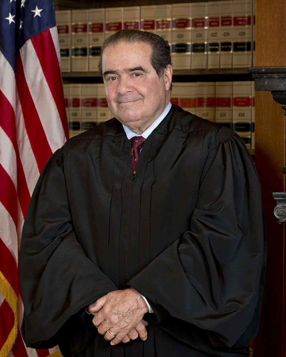 The late U.S. Supreme Court Justice Antonin Scalia is featured posing in front of the American flag.