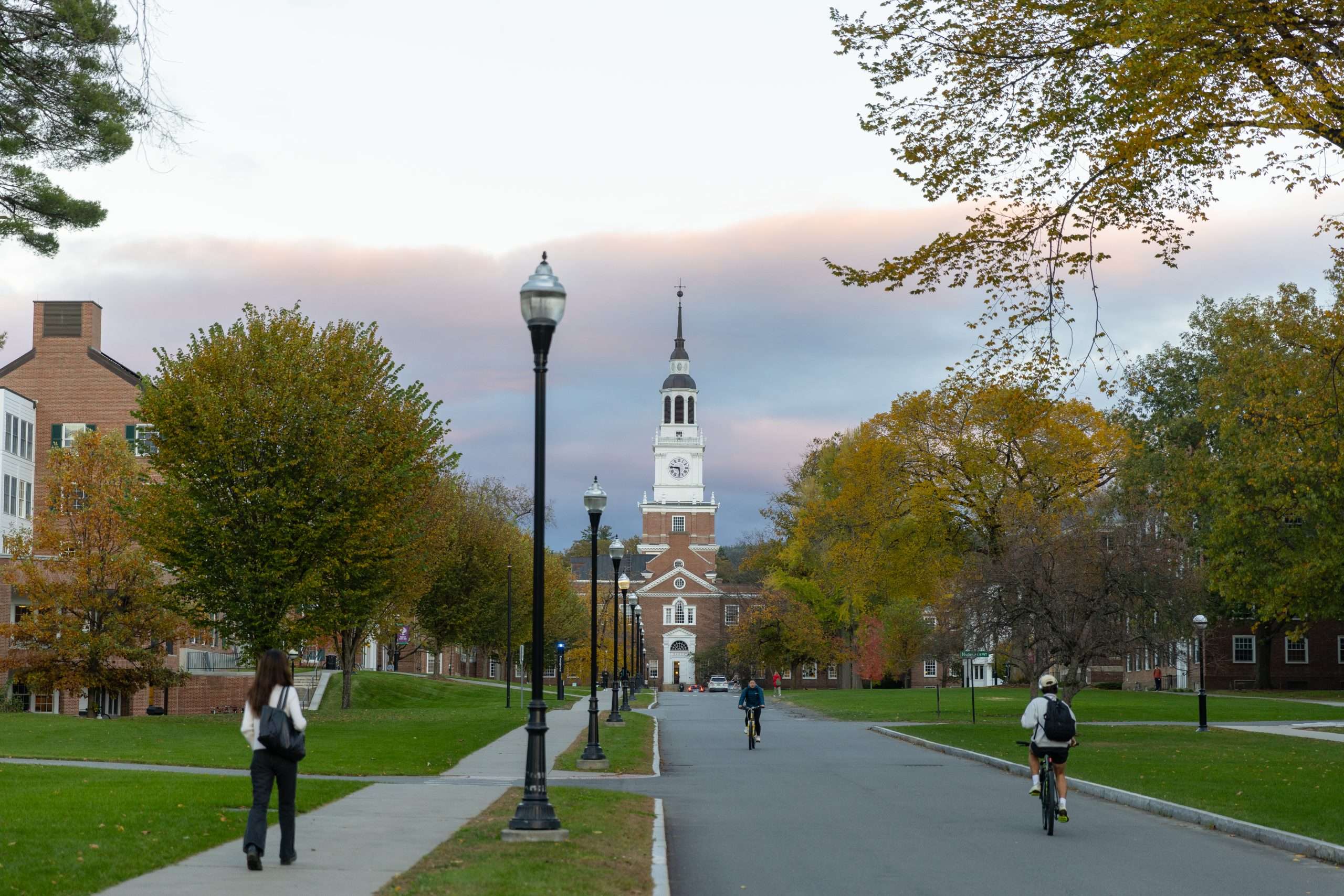 Students bike down the road at Dartmouth College in front of Baker Library