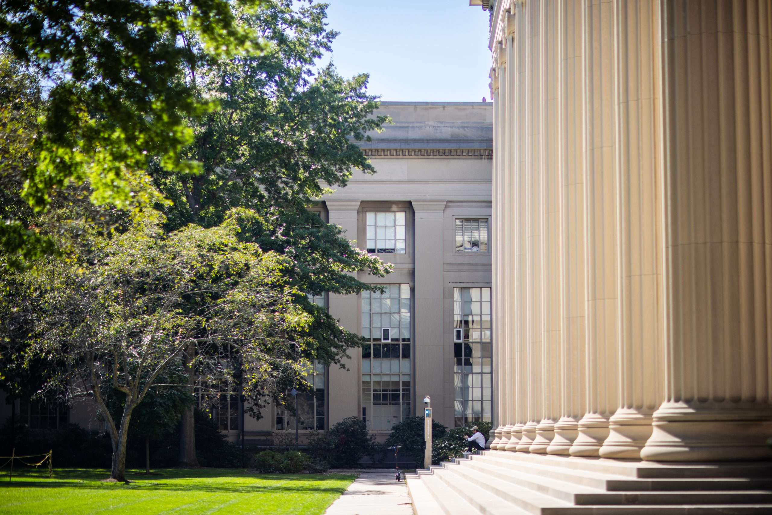 A student sits on the steps of a columned building at MIT.