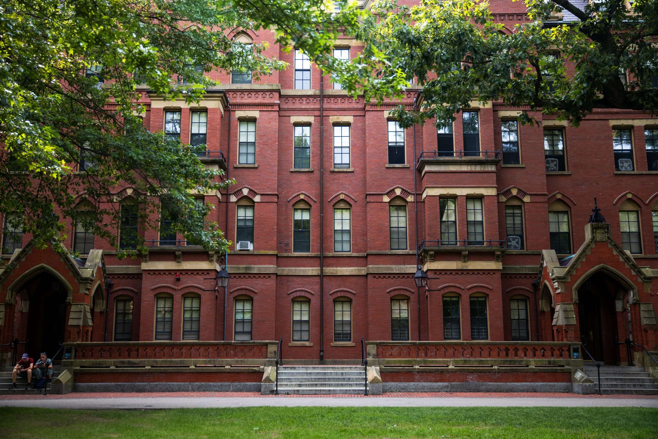 A red brick building is featured at Harvard University beyond a patch of grass.