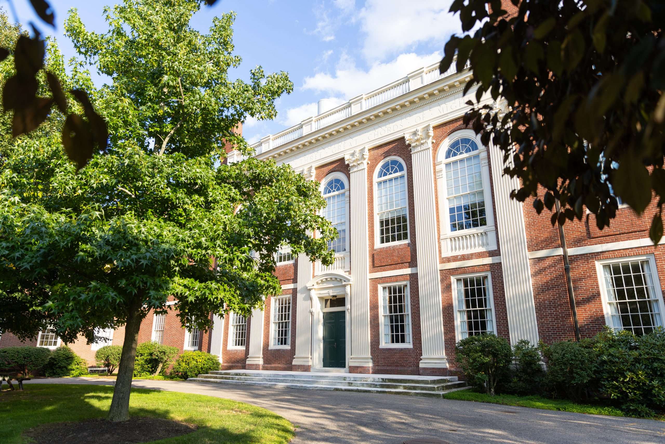 A brick building with a green door is featured beyond a lawn at Harvard University.
