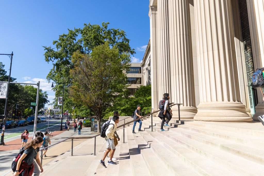 Students walk up steps outside a columned building at MIT.