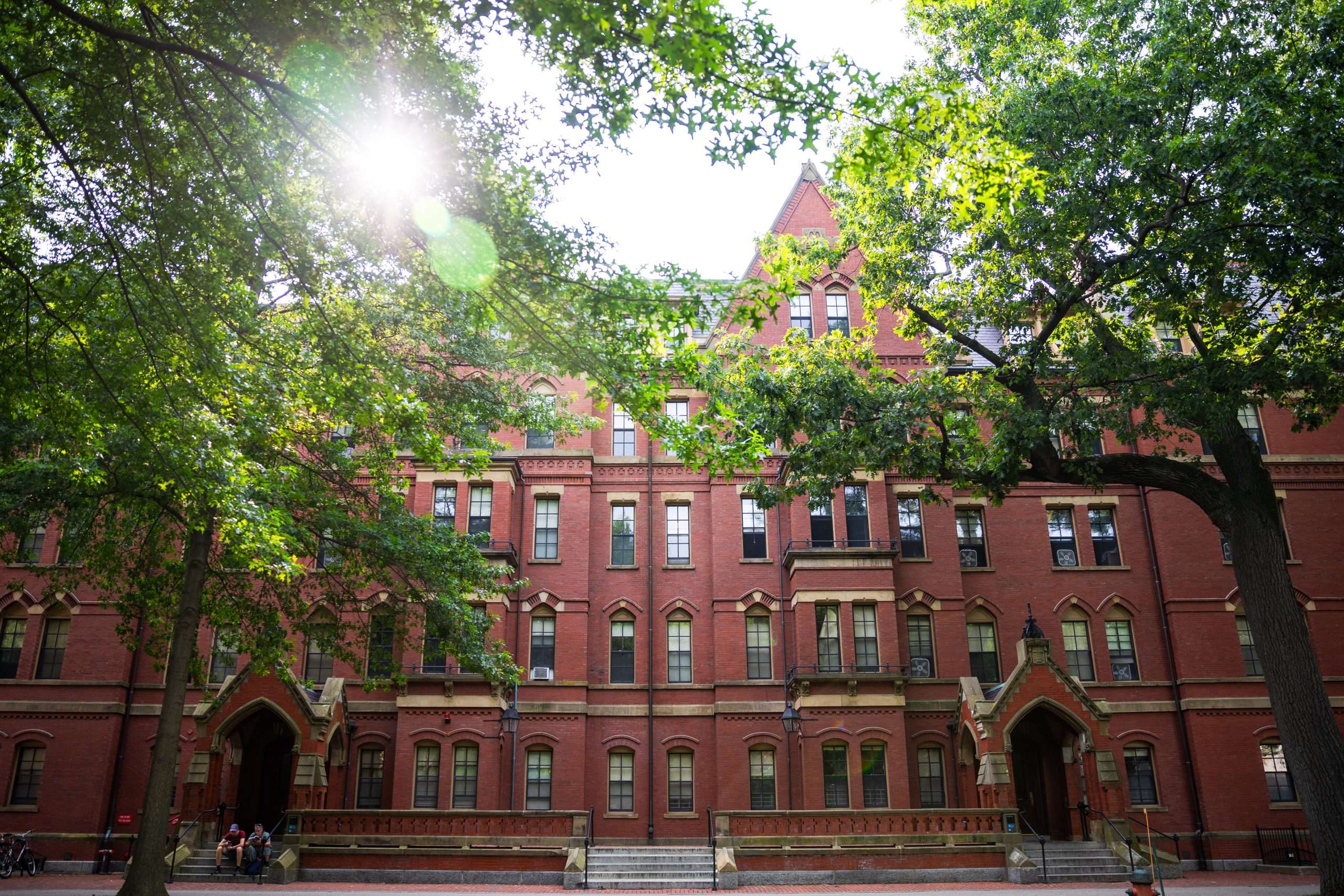 A red brick building at Harvard University is featured beyond trees.