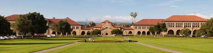 A panoramic of Stanford University's campus, featuring red-roofed buildings beyond a lush green.