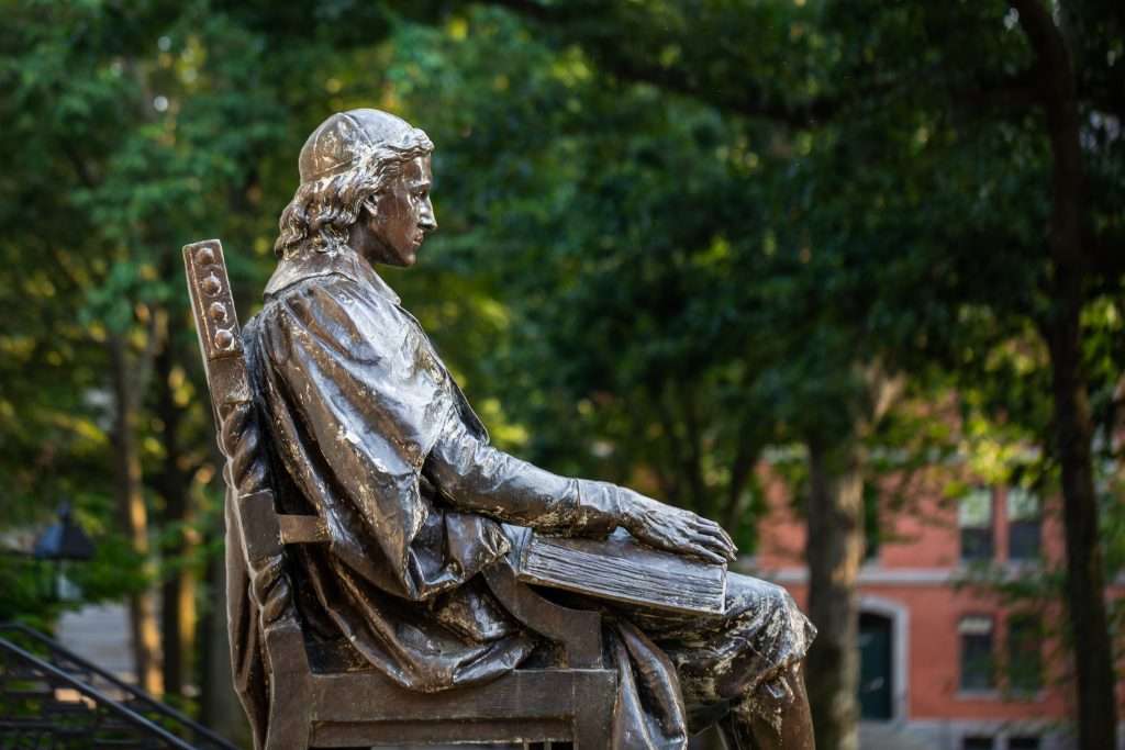 A bronzed statue of John Harvard is visible from the side.