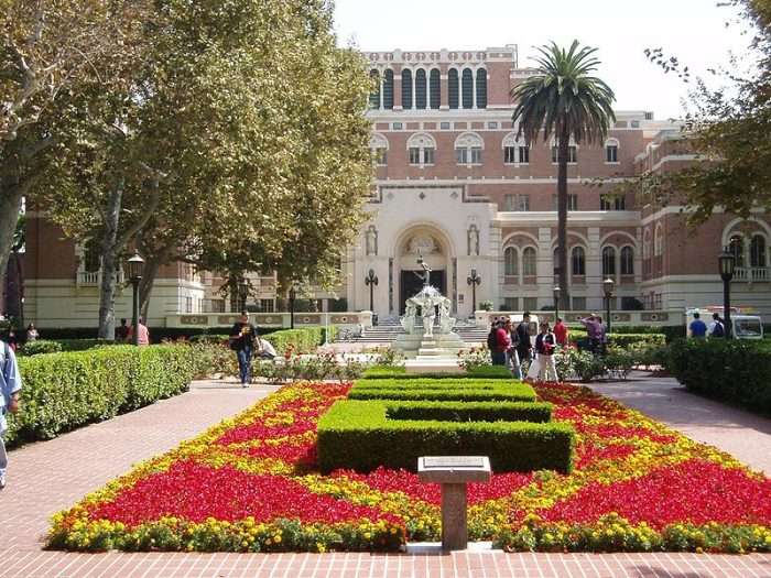 A red and yellow flower garden lies before a red brick building at USC.