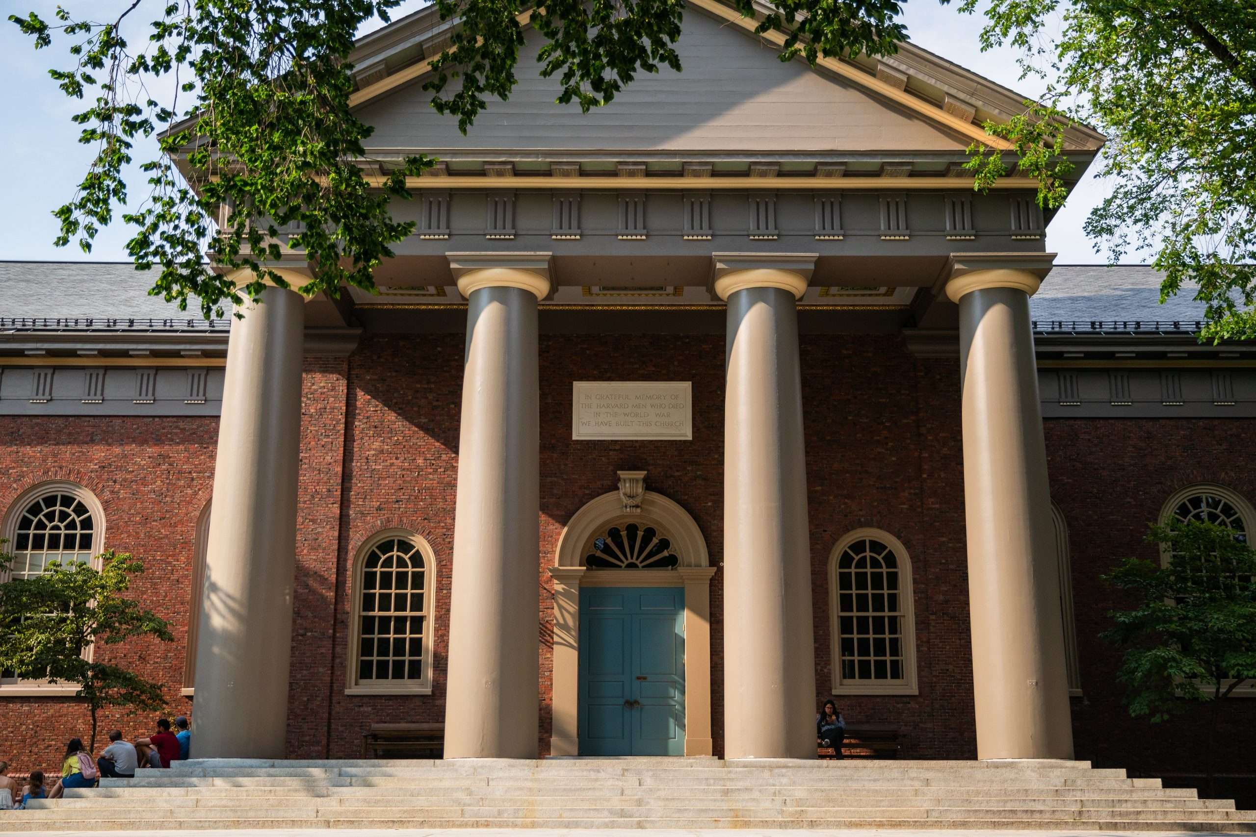 A red brick building with columns and a blue door is featured at Harvard University.
